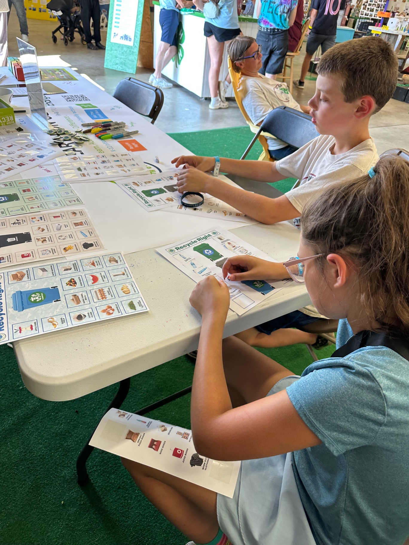Two kids matching item cards to the correct recycling, compost, and trash bins